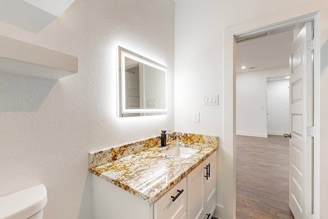 bathroom featuring a textured wall, vanity, wood finished floors, and toilet