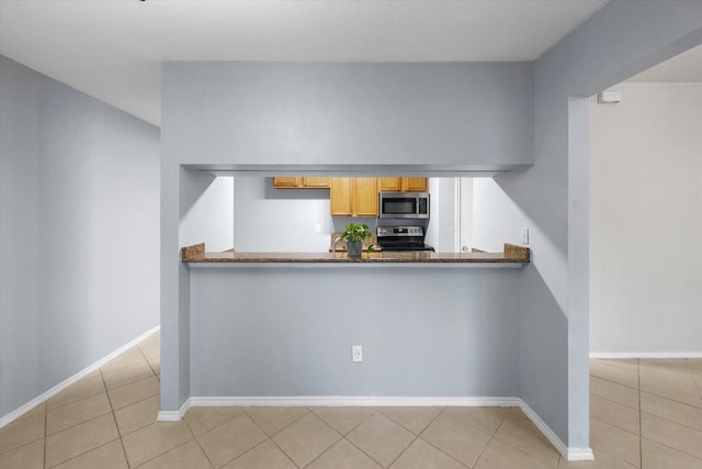 kitchen with a peninsula, light tile patterned floors, baseboards, and appliances with stainless steel finishes