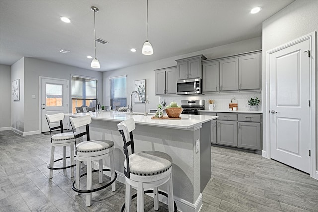 kitchen with a center island with sink, visible vents, gray cabinetry, stainless steel appliances, and a kitchen bar