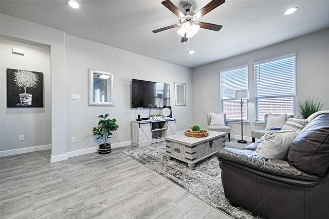 living area featuring a textured ceiling, a ceiling fan, light wood-style floors, and baseboards