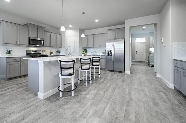 kitchen featuring light wood-type flooring, tasteful backsplash, appliances with stainless steel finishes, and gray cabinets