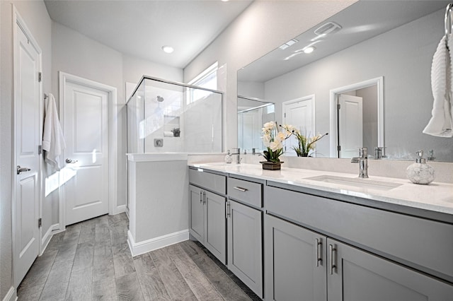 full bathroom with a sink, wood finished floors, a stall shower, and double vanity