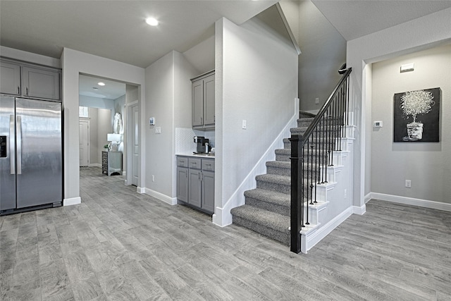 kitchen featuring gray cabinets, stainless steel refrigerator with ice dispenser, recessed lighting, light wood-style floors, and baseboards