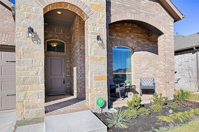 view of exterior entry with a porch, brick siding, and stone siding