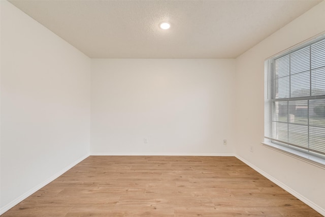 spare room with light wood-style flooring, baseboards, and a textured ceiling