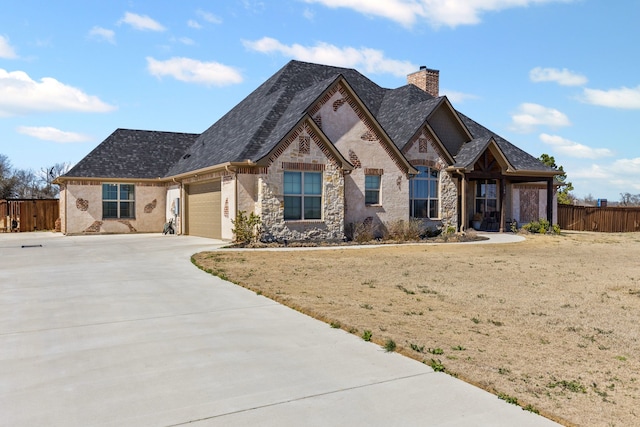 french provincial home featuring roof with shingles, a chimney, concrete driveway, fence, and a garage