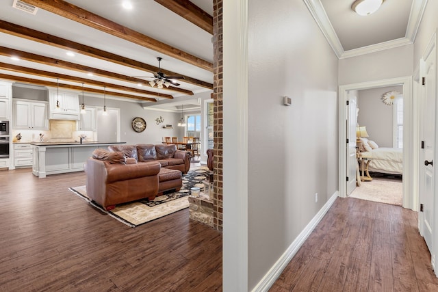 corridor with beam ceiling, dark wood finished floors, visible vents, ornamental molding, and baseboards