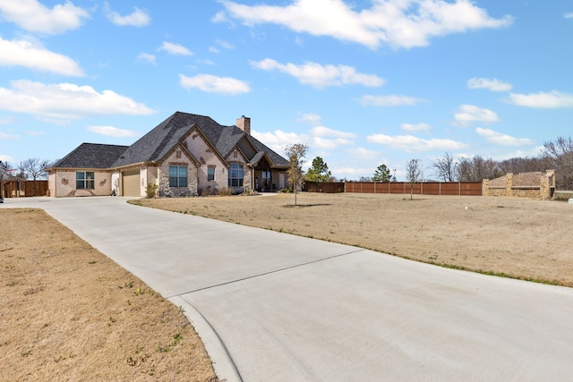 french country inspired facade featuring stone siding, a chimney, concrete driveway, and fence