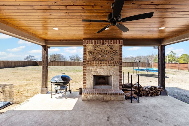 view of patio with a trampoline, an outdoor stone fireplace, a fenced backyard, and grilling area