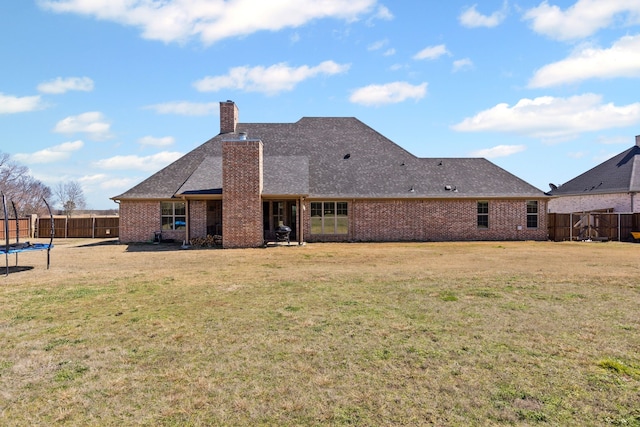 rear view of property featuring a chimney, a trampoline, fence, a yard, and brick siding