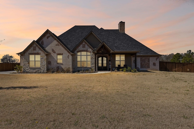 french country style house with fence, stone siding, french doors, a lawn, and a chimney