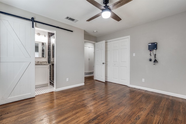 unfurnished bedroom featuring a barn door, visible vents, and wood finished floors