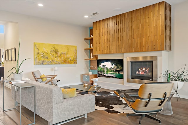 living area with visible vents, recessed lighting, a glass covered fireplace, and wood finished floors