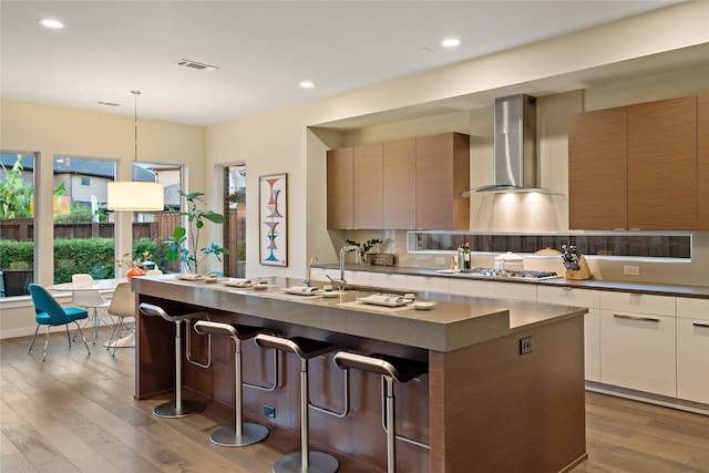 kitchen featuring wall chimney range hood, modern cabinets, visible vents, and stainless steel gas stovetop