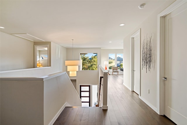 hall with an upstairs landing, recessed lighting, dark wood-type flooring, and baseboards