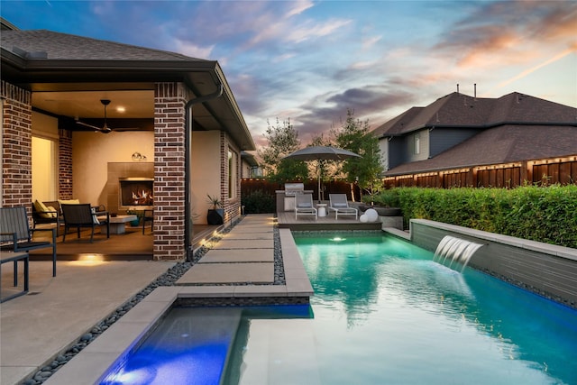 view of pool featuring ceiling fan, a patio area, fence, and a lit fireplace