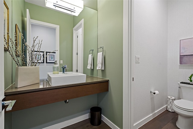 bathroom featuring a wall unit AC, toilet, wood finished floors, and baseboards