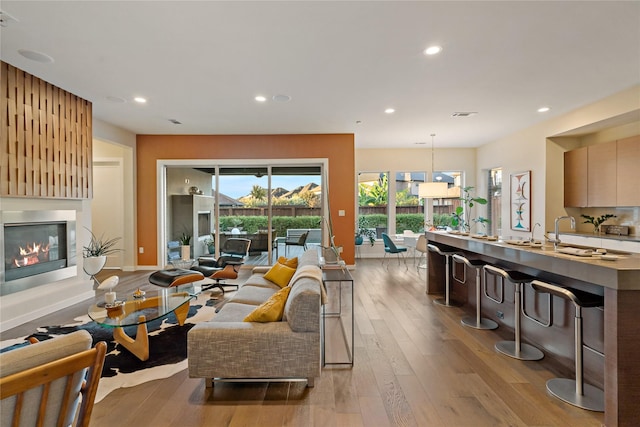 living room with visible vents, a glass covered fireplace, recessed lighting, light wood-style floors, and baseboards