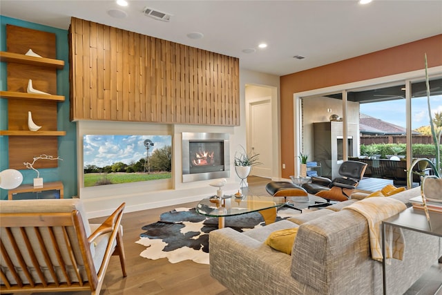 living room with visible vents, recessed lighting, wood finished floors, and a glass covered fireplace