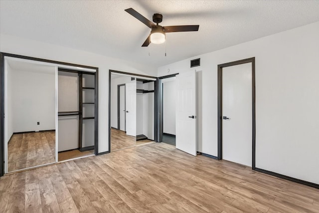 unfurnished bedroom with light wood-style flooring, visible vents, multiple closets, and a textured ceiling