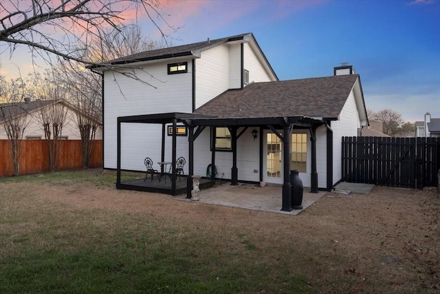 rear view of house with a lawn, a patio, a fenced backyard, a shingled roof, and a chimney