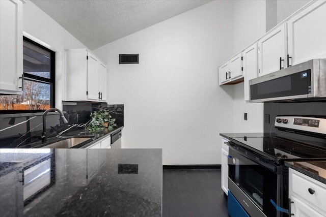 kitchen featuring lofted ceiling, white cabinets, appliances with stainless steel finishes, and a sink