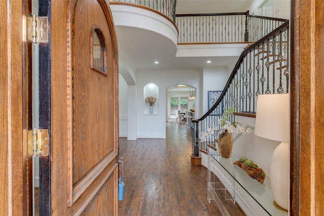 entryway featuring arched walkways, wood finished floors, baseboards, ornamental molding, and stairway