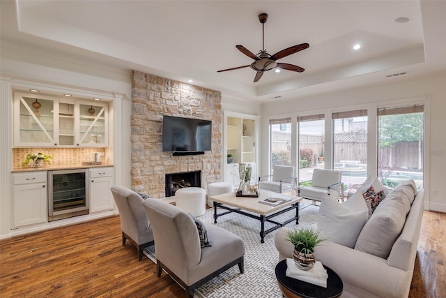 living room featuring beverage cooler, visible vents, a raised ceiling, wood finished floors, and a fireplace