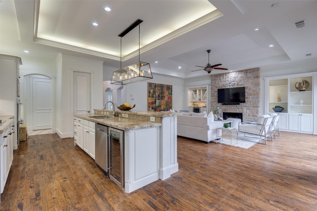 kitchen with ceiling fan, dark wood-type flooring, a fireplace, a sink, and a raised ceiling