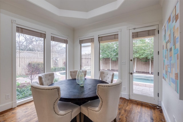 dining space with crown molding, baseboards, a raised ceiling, and wood finished floors