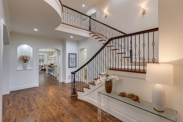 staircase with baseboards, arched walkways, wood finished floors, a high ceiling, and recessed lighting