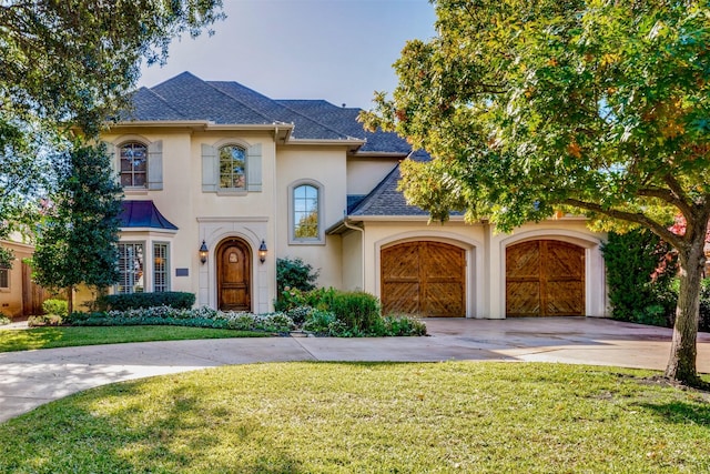 view of front facade featuring roof with shingles, driveway, a front lawn, and stucco siding