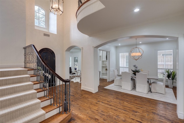 entrance foyer featuring arched walkways, wood finished floors, visible vents, stairs, and an inviting chandelier