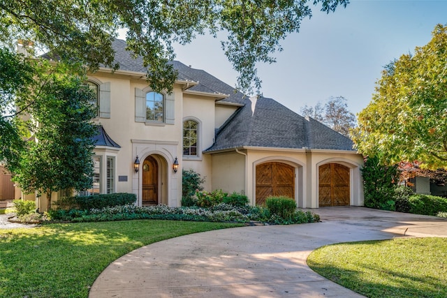 view of front of home featuring driveway, stucco siding, a front lawn, and roof with shingles