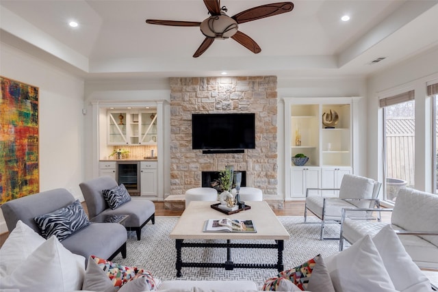 living area featuring a dry bar, beverage cooler, a tray ceiling, light wood-style floors, and a fireplace