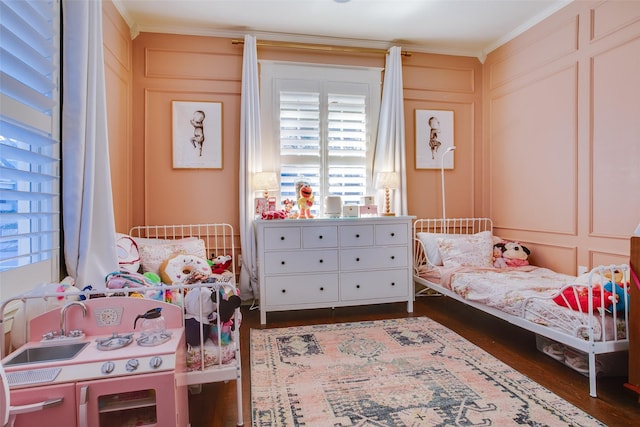 bedroom with crown molding, a decorative wall, and dark wood-style flooring