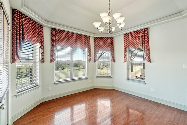 empty room featuring hardwood / wood-style floors, baseboards, an inviting chandelier, and ornamental molding