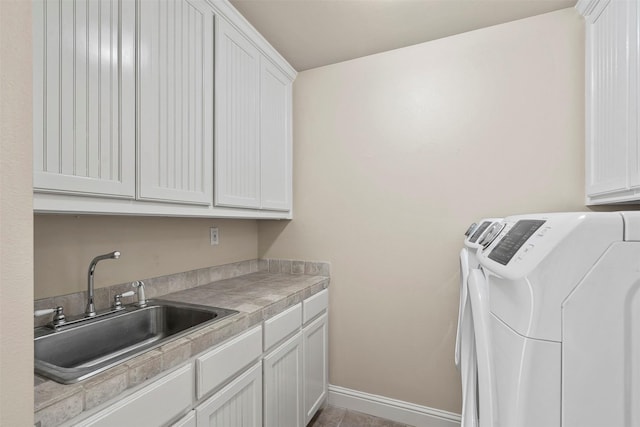 clothes washing area featuring a sink, baseboards, cabinet space, and washing machine and clothes dryer