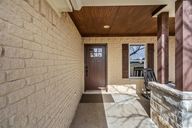 entrance to property featuring a porch and brick siding