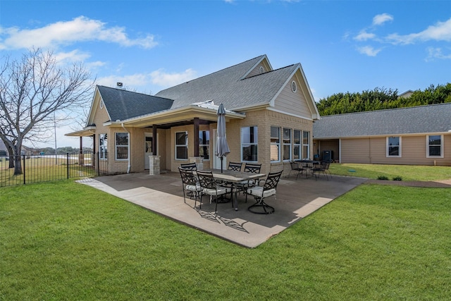 back of property featuring brick siding, a shingled roof, fence, a lawn, and a patio area