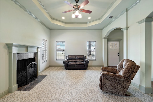 living area featuring a tray ceiling, visible vents, arched walkways, and ornamental molding