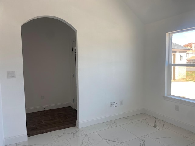 unfurnished room featuring a wealth of natural light, marble finish floor, arched walkways, and baseboards