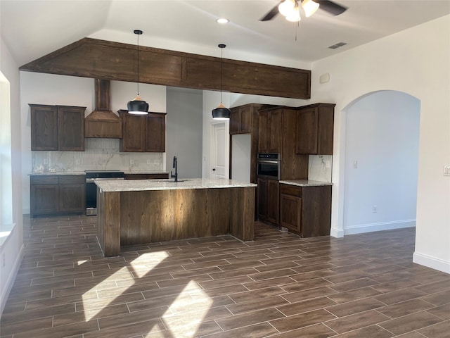 kitchen with arched walkways, range, custom range hood, oven, and backsplash