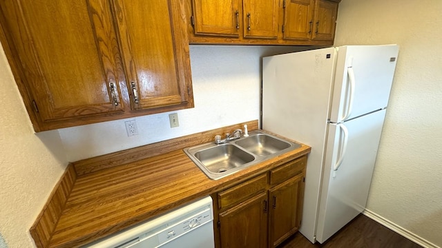 kitchen with white appliances, baseboards, a textured wall, brown cabinets, and a sink