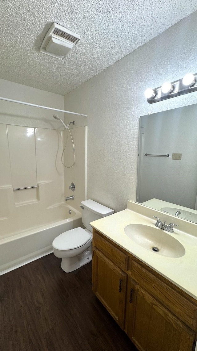 bathroom featuring a textured ceiling, toilet, wood finished floors, vanity, and shower / bathing tub combination