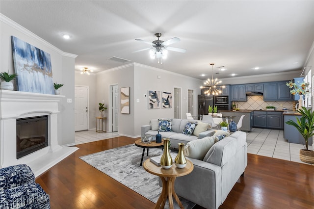 1503 Norway Pine St, Arlington, TX 76012 - living room featuring a chandelier, light wood finished floors, a glass covered fireplace, ceiling fan, and crown molding