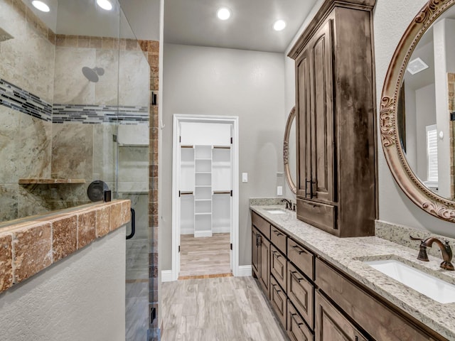 full bathroom with wood finished floors, a sink, a walk in closet, and a shower stall