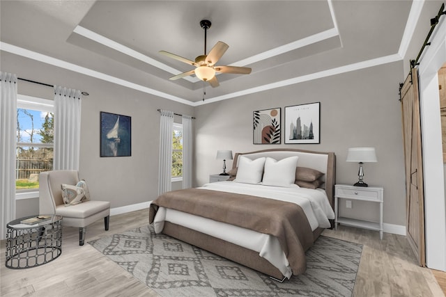 bedroom with a raised ceiling, baseboards, light wood finished floors, and a barn door