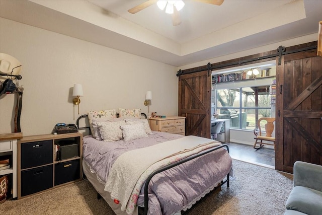 bedroom with a barn door, a raised ceiling, and a ceiling fan