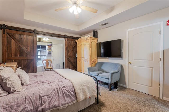 bedroom with carpet floors, a barn door, visible vents, and a tray ceiling